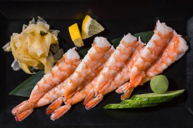 Shrimps on a leaf with cucumber, wasabi, lemon and ginger on a black background