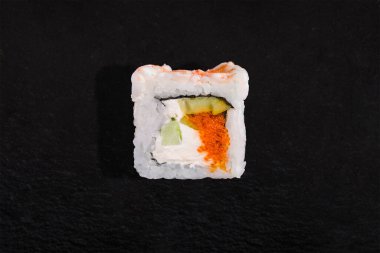 Rolls with crab meat, rice, nori, cream cheese, cucumber and tobiko caviar on a stone black background