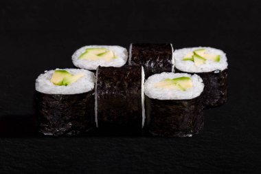 Rolls with nori, rice and avocado on black stone background