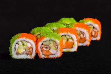 Rolls with nori, green and orange tobiko caviar, eel, cucumber, salmon and squid on a black stone background