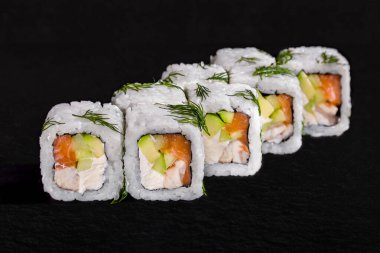 Rolls with dill, rice, nori, cream cheese, cucumber and avocado on a black stone background