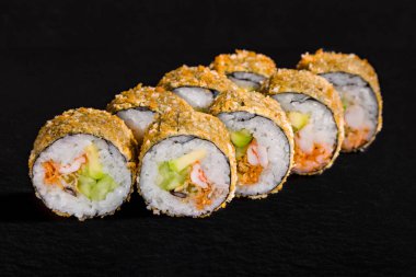 Warm breaded roll with nori, rice, cucumber, avocado, shrimp, octopus and sauce on a black stone background