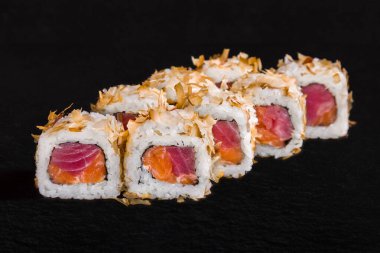 Rolls with rice, tuna, salmon and sprinkles on a black stone background