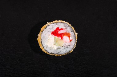 Warm breaded roll with nori, rice, shrimp, cucumber, tobiko caviar, cream cheese and pepper on a black stone background