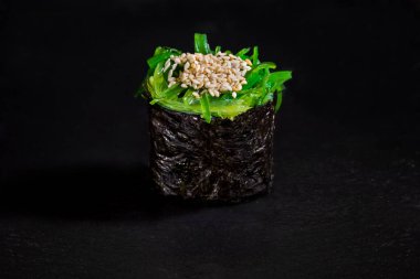 Roll with sesame seeds, chuka and nori on a black stone background