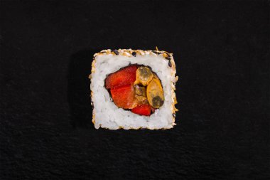 Roll with sesame seeds, rice, pepper and omelet on a black stone background