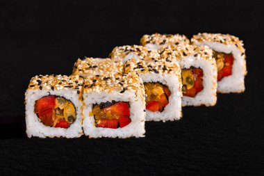 Roll with sesame seeds, rice, pepper and omelet on a black stone background