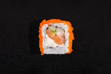 Roll tobiko caviar, rice, cream cheese, cucumber and salmon on a black stone background