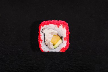 Rolls with tobiko caviar, rice, nori, cream cheese, eel, avocado and fruit on a black stone background
