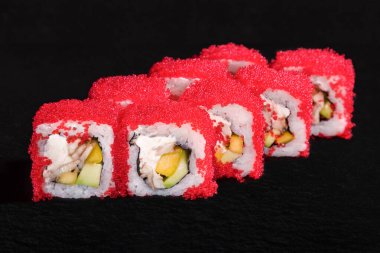 Rolls with tobiko caviar, rice, nori, cream cheese, eel, avocado and fruit on a black stone background