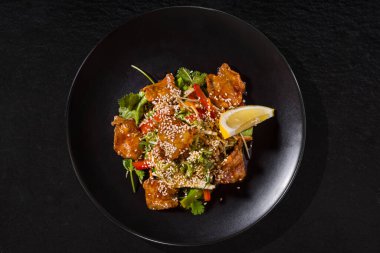 Fried fish with lemon, sesame seeds, parsley and pepper on a black stone background