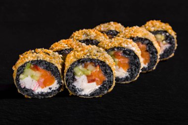 Warm breaded roll with black rice, cream cheese, crab meat, salmon, pepper and tobiko caviar on a black stone background