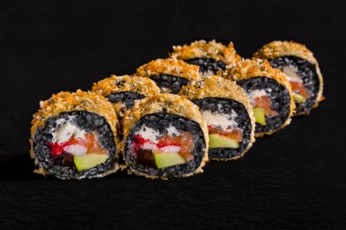 Warm breaded roll with black rice, cream cheese, mushrooms, salmon, pepper and tobiko caviar on a black stone background