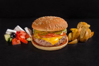 Domuz pirzolası, peynir, domates, salatalık, sos, feta peyniri, zeytin ve kızarmış patatesle siyah bir arkaplanda.