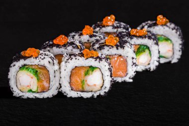 Roll with salmon caviar, black tobiko caviar, cream cheese, eel, shrimp, chuka and salmon on a black stone background