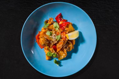 Fried fish with sesame seeds, lemon, mushrooms and pepper on a blue plate on a black stone background