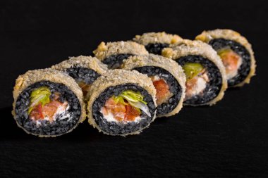 Warm breaded roll with black rice, lettuce, pepper, shrimp and cream cheese on a black stone background