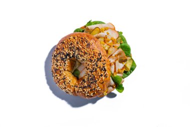 Bun with sesame seeds, salad, pork, mustard, pickled cucumbers and sauce on a white plate