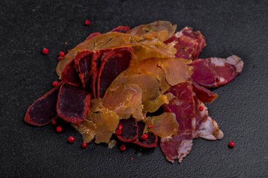 Basturma, jamon and dried chicken with red peppercorns on a stone background. Horizontal orientation