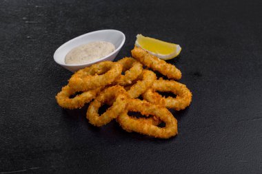 Onion rings in batter with sauce and lemon on a stone background. Horizontal orientation