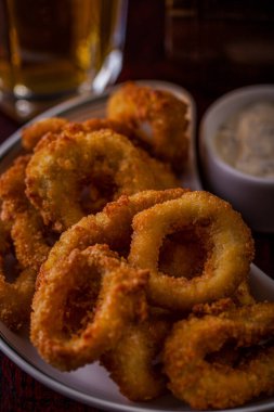 Onion rings in batter with sauce on a wooden board with a glass of beer. Vertical orientation