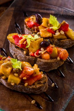 Fırında kırmızı biber, sarı biber, zeytin, çam fıstığı, kabak ve kişniş yapraklı üç çavdar ciabatta bruschetta. Hughchetta cam, şeffaf tabak ve balzamik sosun üzerinde duruyor..