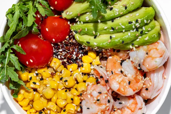 Bowl with shrimp. On a white background in a white ceramic bowl are slices of avocado, quinoa, cherry tomatoes, shrimp and corn. Topped with white and black sesame seeds.