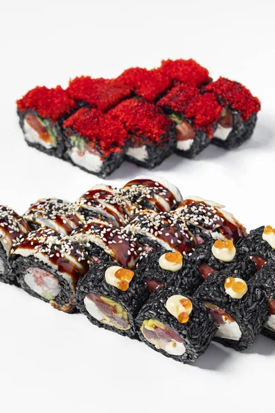 Black Friday sushi set. Three sets of black rice and cuttlefish ink stand on a white background. Sushi with tuna, mango, Philadelphia cheese, tofu, wrapped in nori, black rice, Japanese mayonnaise and red salmon caviar on top. Nearby is a sushi roll