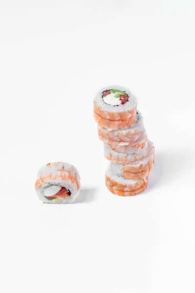 Sushi tiger dragon with shrimp. Filled with salmon, avocado, red tobiko caviar, wrapped in nori seaweed, rice and tiger shrimp. The roll in the form of a tower stands on a white background, next to it, on its side, there is a piece of sushi stuffed i
