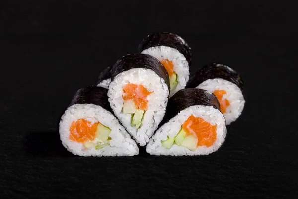 Rolls with nori, rice, salmon and cucumber on a stone black background