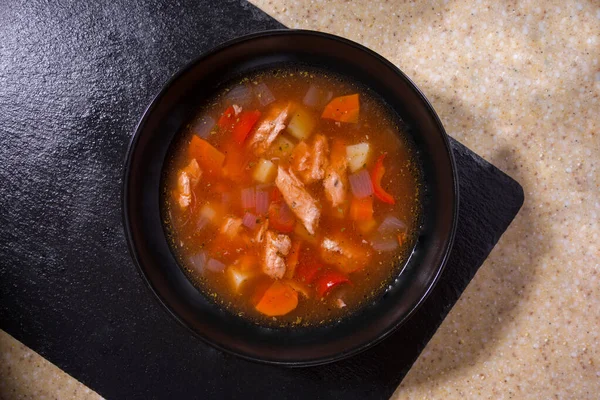 Plate of soup with carrots, meat, onions and peppers on a black and white background