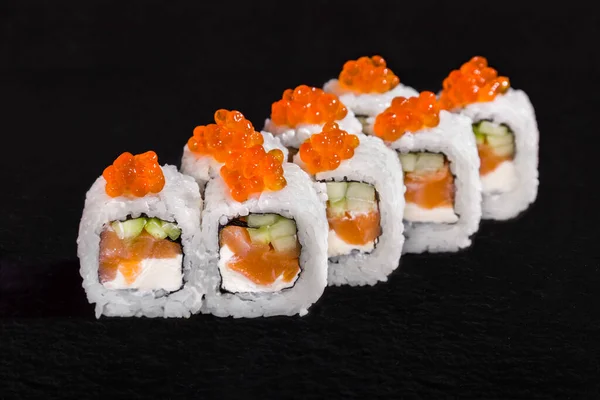 Rolls with caviar, rice, nori, cucumber, cream cheese and salmon on a black stone background
