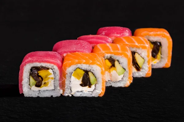 Rolls with tuna, salmon, rice, nori, mushrooms, fruit, avocado and cream cheese on a black stone background