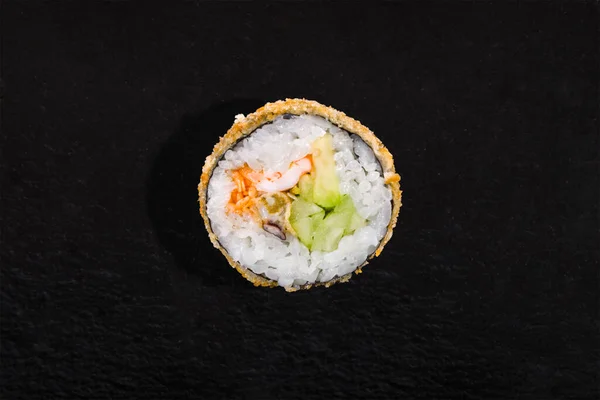 Warm breaded roll with nori, rice, cucumber, avocado, shrimp, octopus and sauce on a black stone background