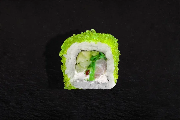 Rolls with green tobiko caviar, rice, nori, tuna, chuka and cucumber on a black stone background
