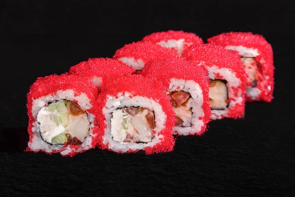 Rolls with tobiko caviar, rice, nori, cream cheese, pepper, squid and cucumber on a black stone background