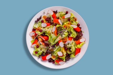 Yengeç sopalı salata, salatalık, kırmızı frenk üzümü, marul ve lahanalar mavi arka planda bir tabakta.