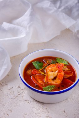 Karides, domates, kızak, fesleğen ve mastürbasyon yapraklı çorba kaba beton ve arka planda beyaz bir bez.