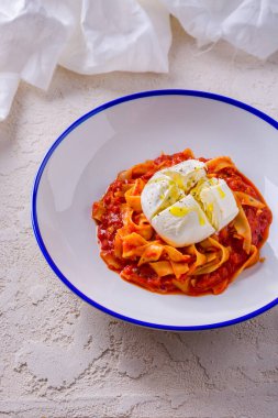 Kıyma, sos ve mozarellalı spagetti kaba betonun üzerinde duruyor ve arka planda beyaz bir bez var.