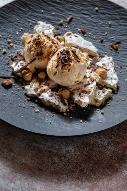 Çikolata parçalı dondurma topları, fındıklar, fıstıklar ve kremalar ahşap bir masada.