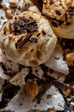 Çikolata parçalı dondurma topları, fındıklar, fıstıklar ve kremalar ahşap bir masada.