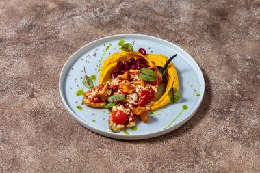 Mercimek püresi, iki yarım fırında patlıcan, domates, paprika ve parmesan peyniri, üstünde chanterelle gibs ve üstünde marul yaprakları. Kaynamış kırmızı fasulye püre üzerinde uzanıyor. Yiyecek mavi, yuvarlak, seramik bir tabakta yatıyor. Tabak duruyor.