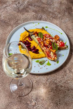 Mercimek püresi, iki yarım fırında patlıcan, domates, paprika ve parmesan peyniri, üstünde chanterelle gibs ve üstünde marul yaprakları. Kaynamış kırmızı fasulye püre üzerinde uzanıyor. Yiyecek mavi, yuvarlak, seramik bir tabakta yatıyor. Tabak duruyor.