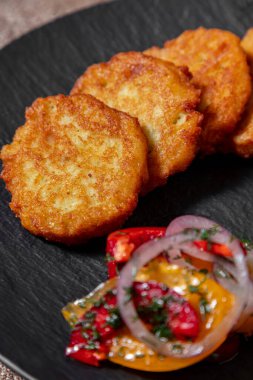 Kızartma tavasında tereyağlı ızgara patates gözlemesi yanında kırmızı soğan, paprika ve domates salatası, ayçiçeği yağı ve ince doğranmış maydanoz serpiştirilmiş. Yakınlarda ekşi kremalı bir seramik kase var. Yiyecekler siyah renkte.