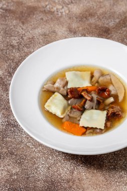 Tavşan mantarlı çorba, porcini mantarı, havuç, mantar ve fesleğen yaprağı. Çorba beyaz, yuvarlak, derin, seramik bir tabağa dökülüyor. Tabak koyu bir arka planda duruyor, kahve rengi..