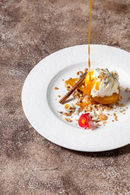 Karamelli ve armut armudu aromalı dondurma. Üzerine karamel dök. Armut beyaz, yuvarlak, seramik bir tabakta yatıyor. Ezilmiş cevizler, etrafa saçılmış mavi peynir, karamel akıntıları, yenilebilir bir menekşe çiçeği ve tarçın çubuğu. Th