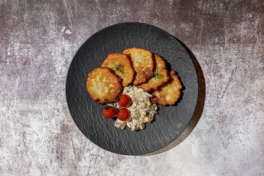 Dereotu tohumlu patates gözlemeleri, gri arka planda soslu kiraz domatesleri ve mantarlar.