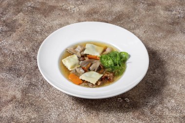 Tavşan mantarlı çorba, porcini mantarı, havuç, mantar ve fesleğen yaprağı. Çorba beyaz, yuvarlak, derin, seramik bir tabağa dökülüyor. Tabak koyu bir arka planda duruyor, kahve rengi..