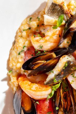 Deniz mahsullü Fregola makarna ve bir bardak gül şarabı. Yemekler beyaz, seramik bir tabakta, çatal bıçak takımı yakınlarda duruyor. Bir tabak makarna beyaz bir masa örtüsünün üzerinde duruyor..