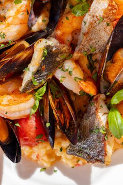 Fregola pasta with seafood and a glass of rose wine. The food lies in a white, ceramic plate, cutlery lies nearby. A plate of pasta sits on a white tablecloth.